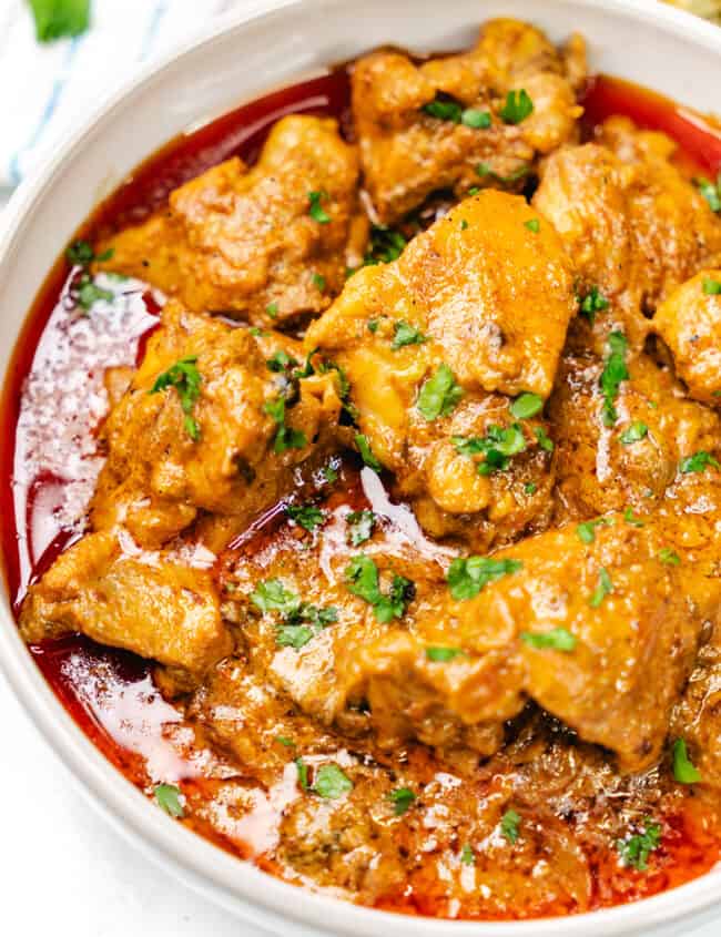 A close-up of Chicken Korma garnished with fresh cilantro in a white bowl.