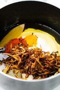 Spices, fried onions, and yogurt in a pot, ready for cooking.