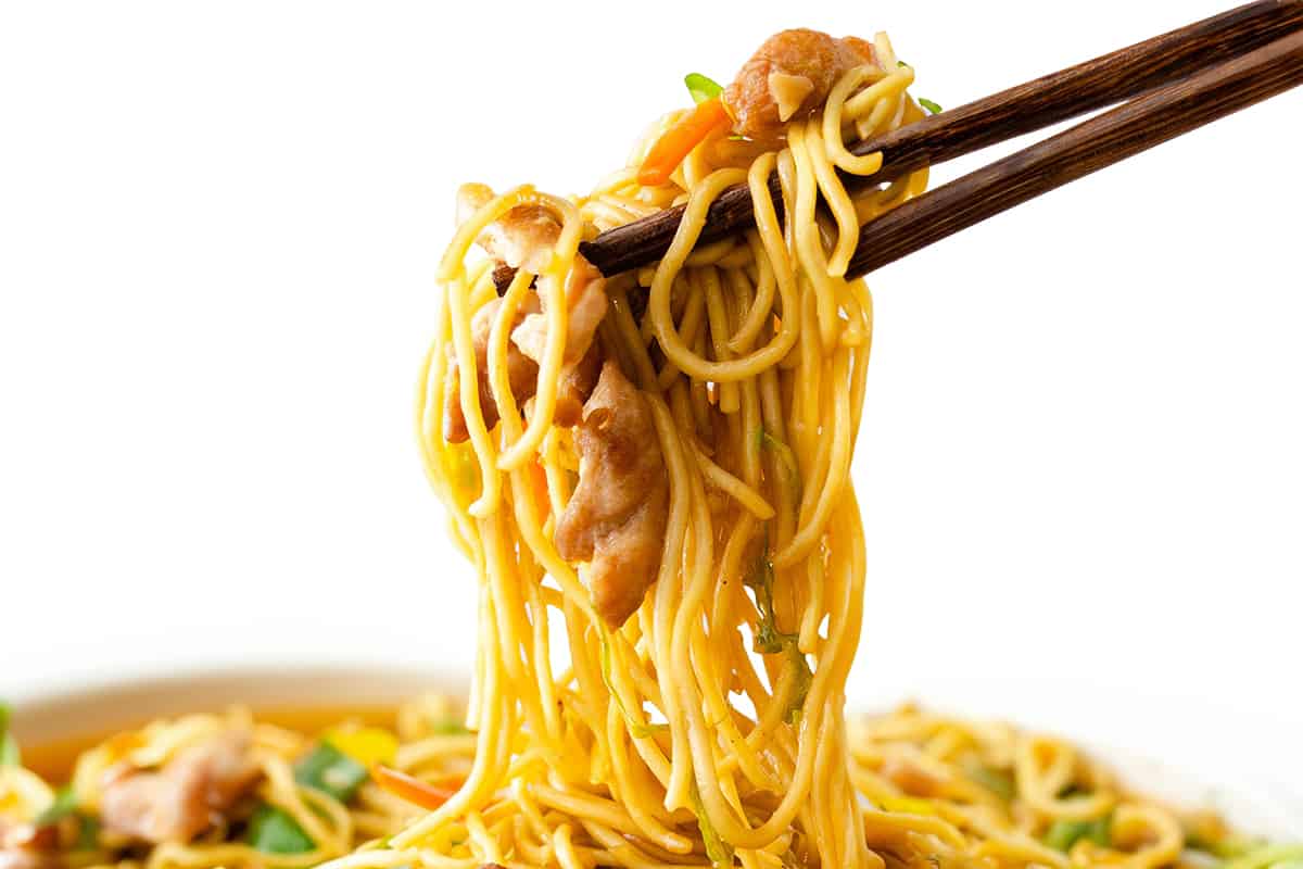 Chopsticks holding a chicken lo mein with noodles, vegetables, and chicken, set against a white background.