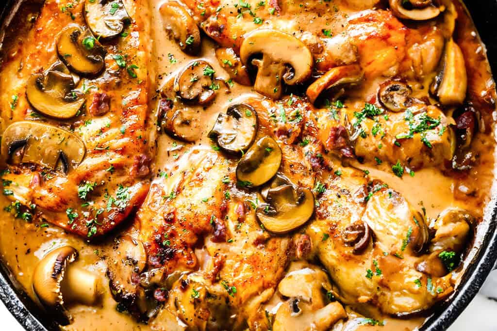 A close up image of A cast iron pan filled with chicken marsala and mushrooms.