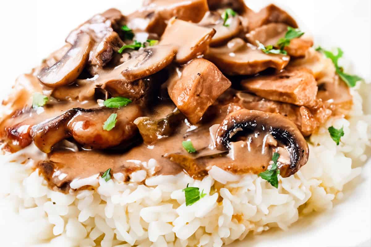 A close up image of Chicken Stroganoff on a white plate with a white background.