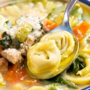 A bowl of comforting Chicken Tortellini Soup, with a spoon.