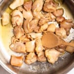 Sautéing bite-sized chicken pieces in a pot with a wooden spoon, showing golden-brown searing.