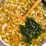 A pot of soup with diced vegetables and chopped parsley, wooden spoon included, indicating a meal in progress.