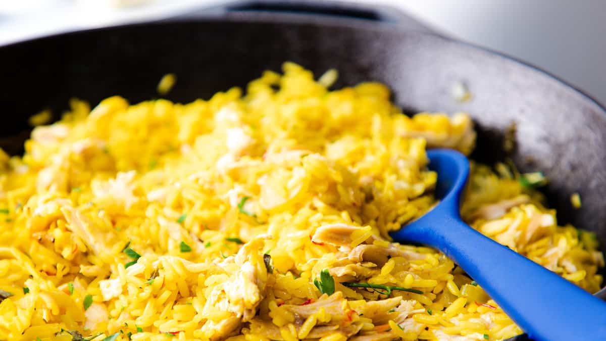 a pan full of Chicken and yellow rice in a black skillet.