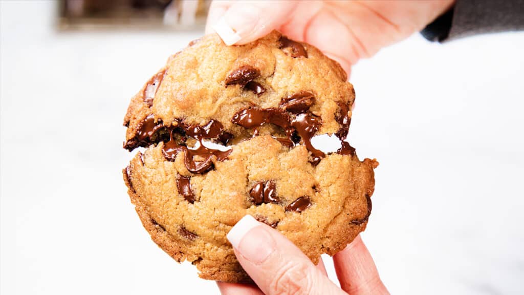 A chocolate chip cookie being broken in half.
