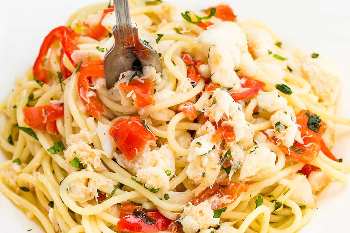 A close up image of a plate of spaghetti with crab, chopped parsley and red peppers.