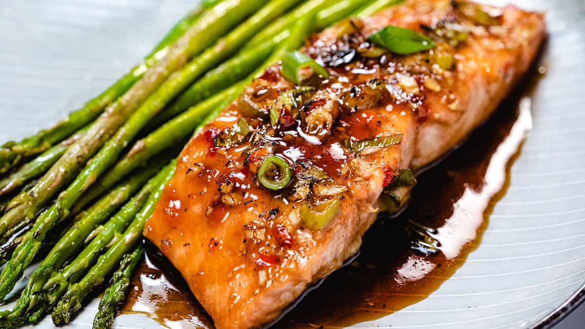 Glazed salmon on a plate with asparagus next to it.