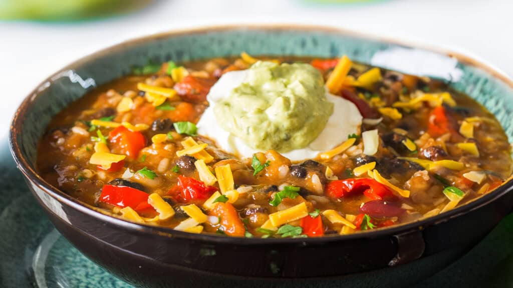 a bowl of Mexican soup topped with Guacamole and sour cream.