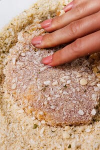 A pork chop being pressed into seasoned breadcrumbs preparing for frying.