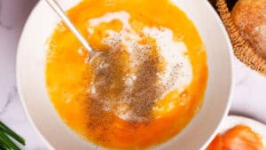 A bowl filled with ingredients for a breakfast dish. The ingredients include eggs, milk, and spices.