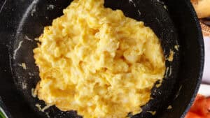 A close-up of a black pan filled with lightly scrambled eggs.