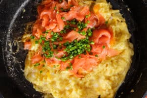 A skillet containing scrambled eggs with chopped smoked salmon and chives mixed in.