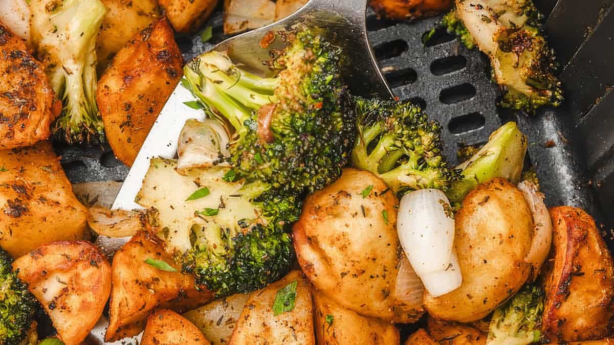 A close up image of air fryer broccoli and potatoes being served from an air fryer.