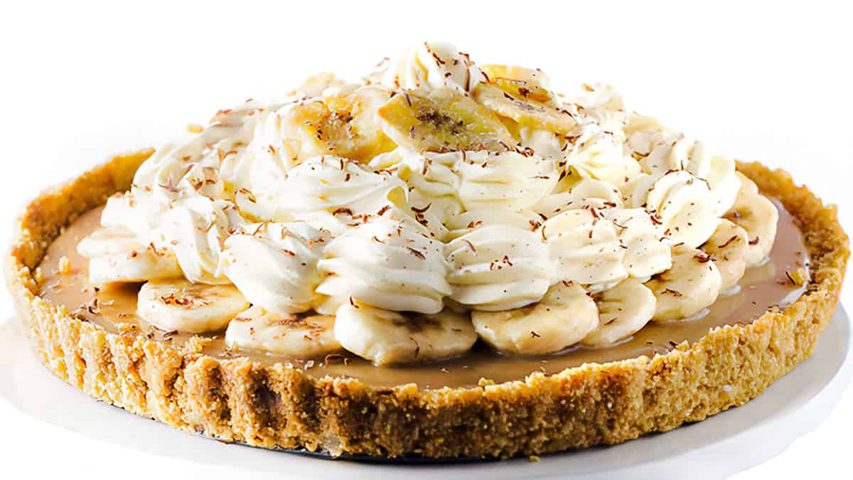 The Banoffee Pie on a cake stand showing the crust, caramel layer, banana layer, whipped cream and banana chips as decoration.