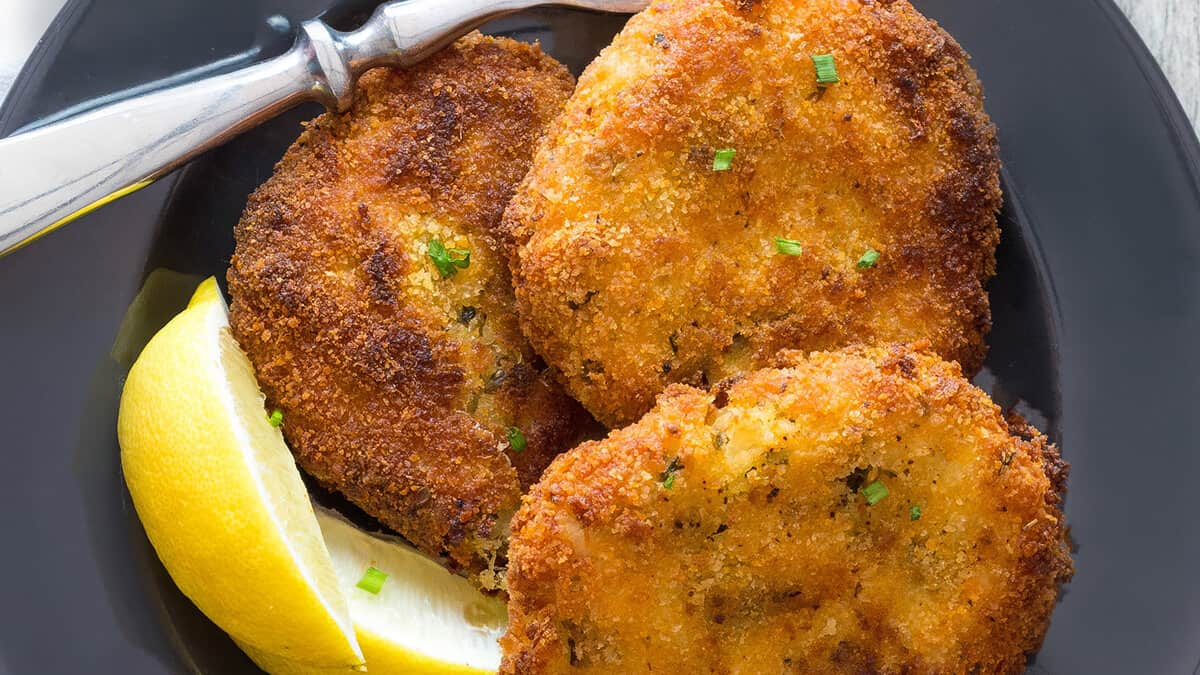 Three Crab Cakes on a plate with lemon wedges and a fork next to it.