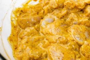 glass bowl filled with chunks of chicken marinating in a vibrant yellow sauce.