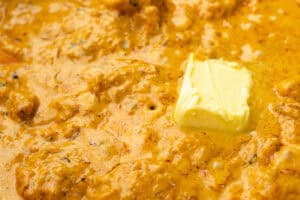 A vibrant yellow curry sauce with tender chicken pieces and a dollop of butter being melted in.