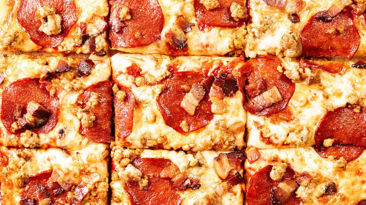 Close-up of several square-cut slices of pizza topped with melted cheese, pepperoni, sausage crumbles, and pieces of bacon—perfect for Beginner Recipes looking for easy and delicious homemade dishes.