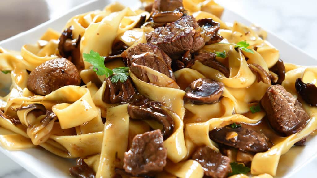 A close up image of a bowl filled with Beef with Mushrooms and noodles.