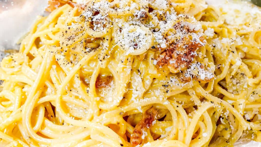 Spaghetti Alla Carbonara piled high on a plate with crisp guanciale.