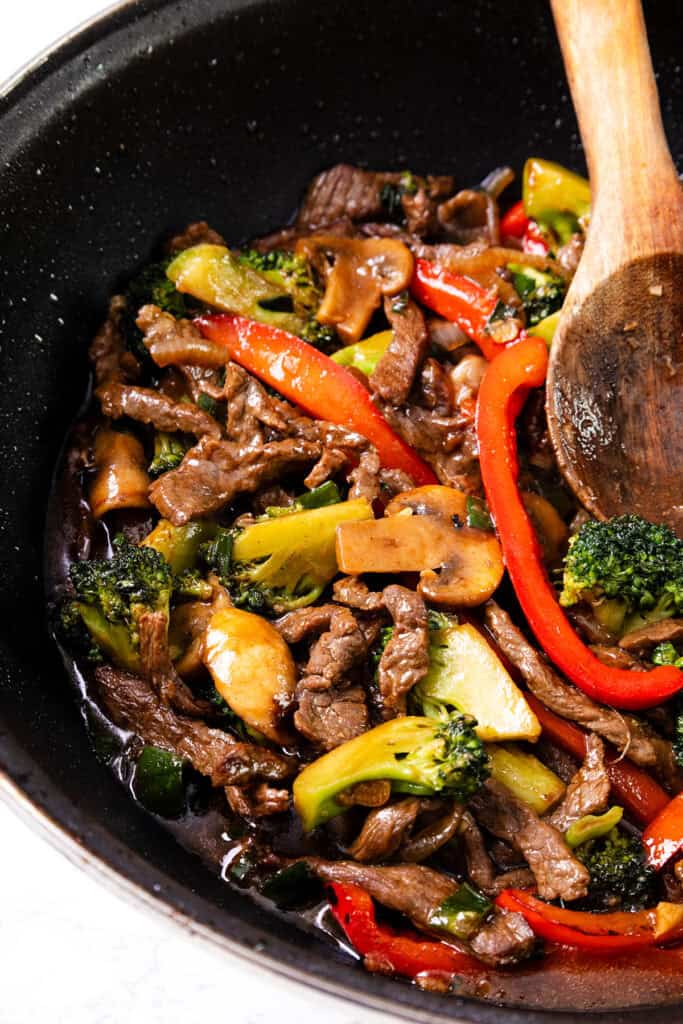 A colorful steak stir fry in a black skillet, featuring thinly sliced beef mixed with broccoli, bell peppers, and mushrooms.