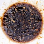 Soy sauce-based marinade mixture in a bowl, featuring ingredients like minced garlic and finely chopped ginger