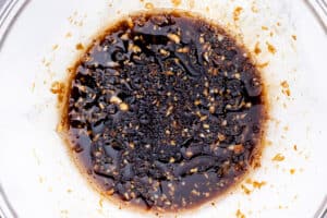 Soy sauce-based marinade mixture in a bowl, featuring ingredients like minced garlic and finely chopped ginger
