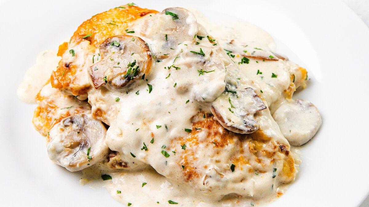 Chicken breast covered in creamy white mushroom sauce, garnished with chopped parsley and served on a white plate—a classic choice for those seeking comforting dinner recipes.