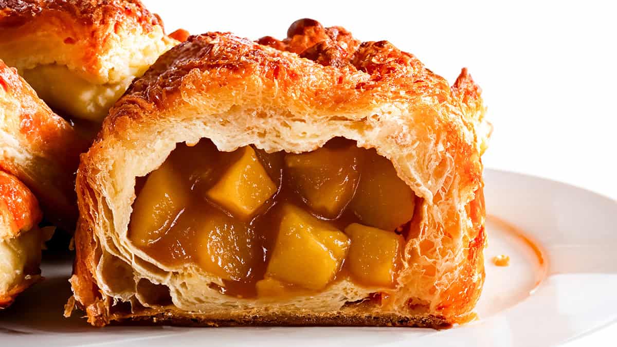 A close-up of a flaky, golden-brown pastry filled with chunks of apple in a glossy caramel sauce, sitting on a white plate—a delicious highlight among classic apple recipes.
