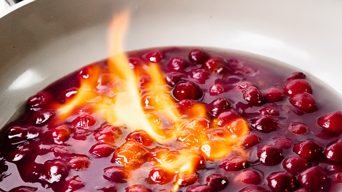 A close-up of cherries simmering in a sauce with visible orange flames, this vibrant scene captures a festive flambé—perfect for adding flair to your Memorial Day Recipes.