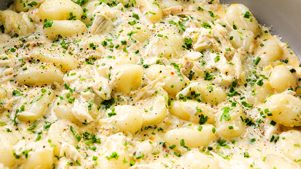 Creamy gnocchi dish topped with chopped herbs, cracked black pepper, and shredded chicken in a rich white sauce—a standout among pasta recipes. The gnocchi are evenly coated and garnished, creating a fresh and appetizing look.