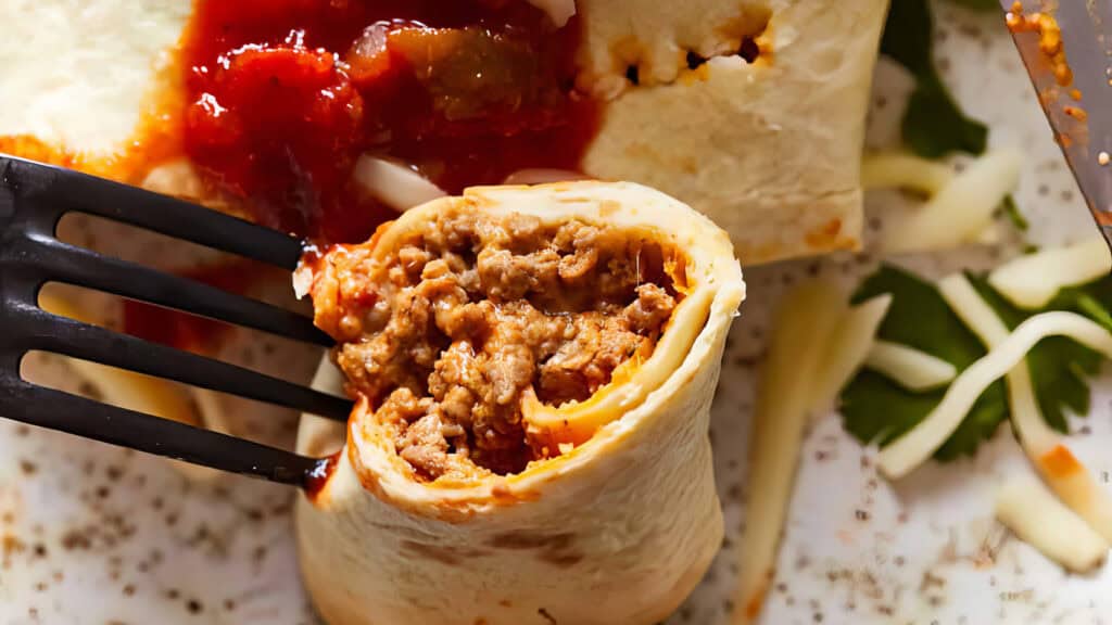 A close-up shot of a Beef Taquito filled with seasoned ground meat. A fork is holding a cut section of the Beef Taquito to show its savory filling.