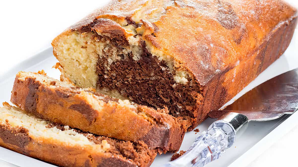 A loaf cake of marble with swirls of chocolate and vanilla, partially sliced on a white platter with a knife beside it—a classic treat from quick bread recipes.