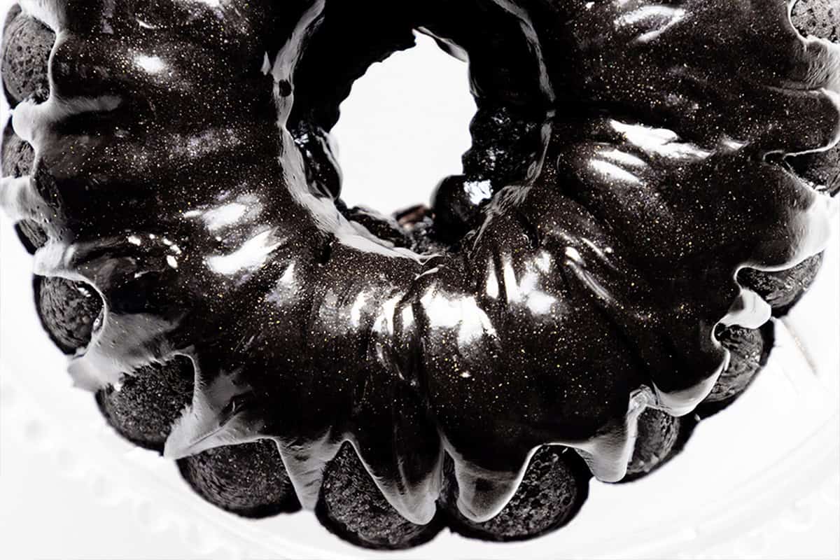 A shiny black velvet bundt cake with a glossy glaze is seen from above. The cake has a rich, dark color, and its smooth surface reflects light, creating an elegant visual effect on a white background.