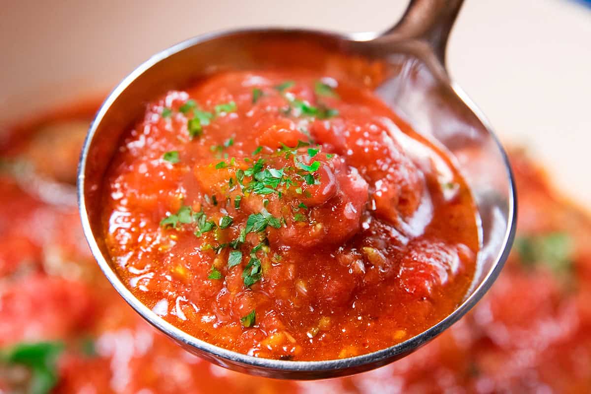 A close-up of a spoonful of chunky tomato sauce, inspired by our 20 Easy Recipes, garnished with chopped parsley and held above a pot of more tomato sauce.