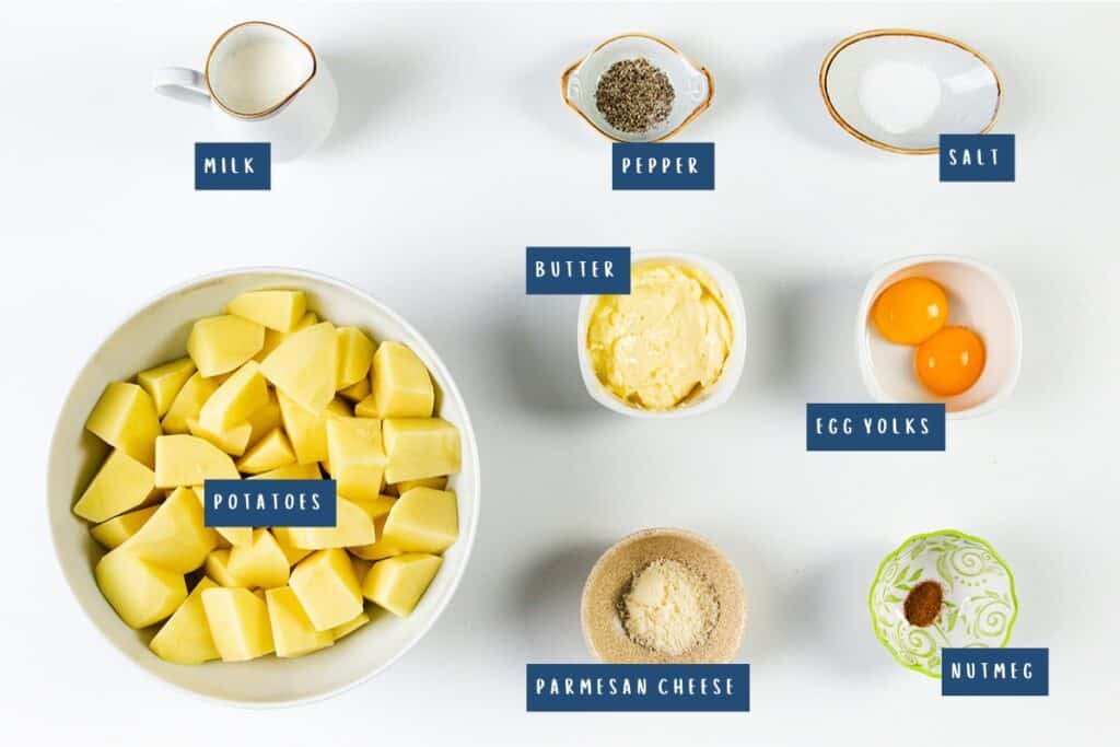The image features ingredients for a delightful Duchess Potatoes recipe. You'll find labeled items: potatoes in a bowl, butter, egg yolks, parmesan cheese, nutmeg, milk, salt, and pepper—each neatly presented in separate dishes.