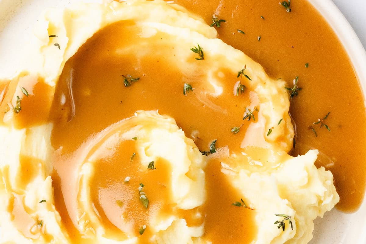 A plate of creamy mashed potatoes topped with rich, make-ahead turkey gravy and garnished with sprigs of fresh thyme. The dish appears smooth and appetizing, inviting a comforting meal experience.