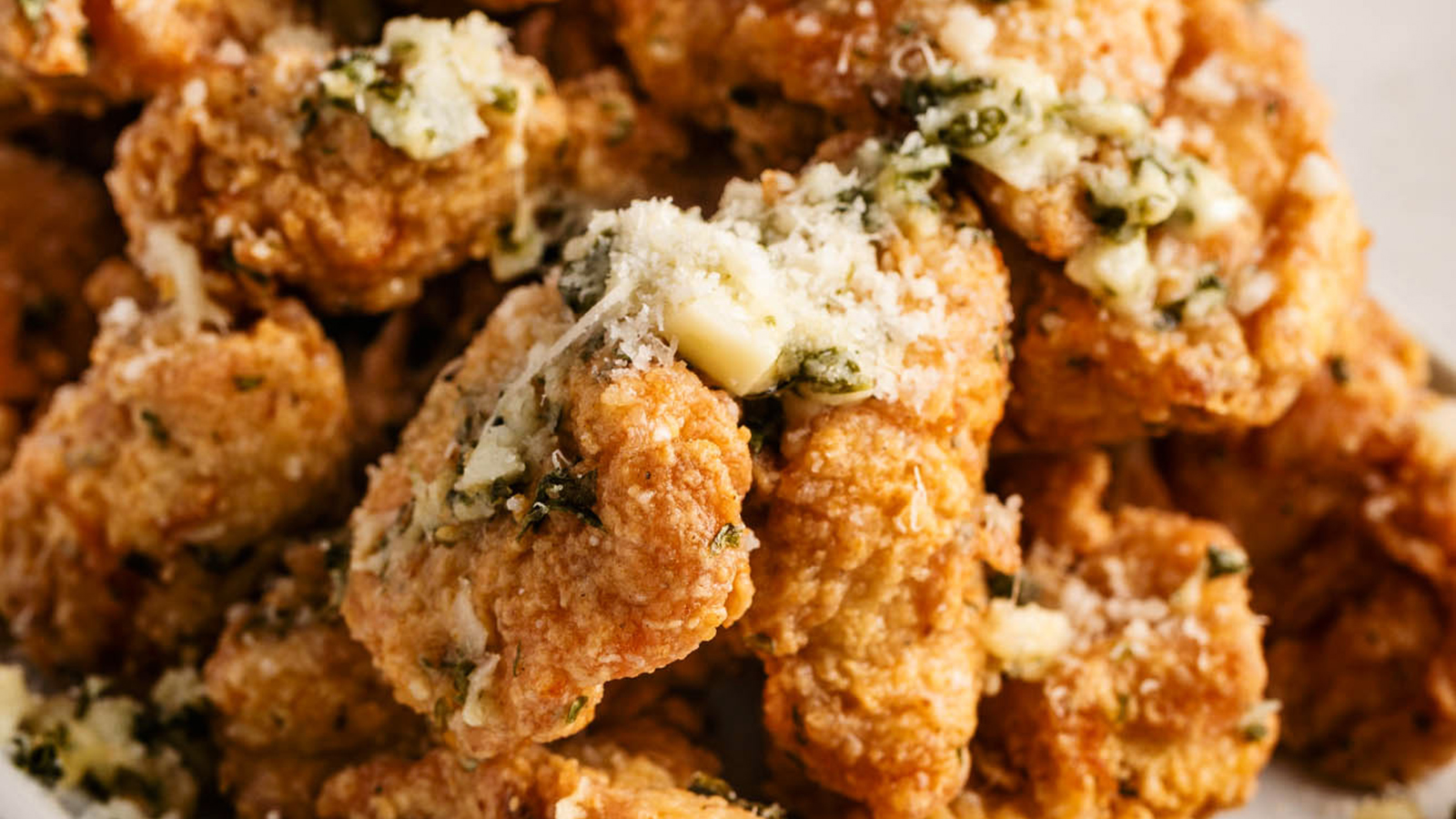 Close-up of a plate of crispy chicken wings, perfect as Thanksgiving appetizers, topped with melted butter, minced garlic, and sprinkled herbs. The golden-brown texture with savory garnishes is clearly visible.
