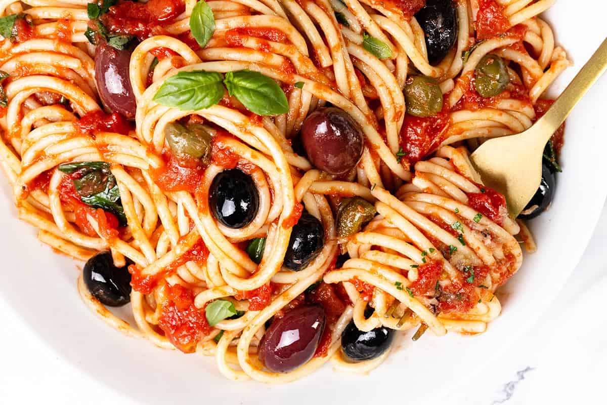 A plate of spaghetti alla puttanesca, a star of pasta dinners, features a rich tomato sauce, black olives, capers, and fresh basil. A fork twirls some pasta, showcasing the vibrant colors of the ingredients.