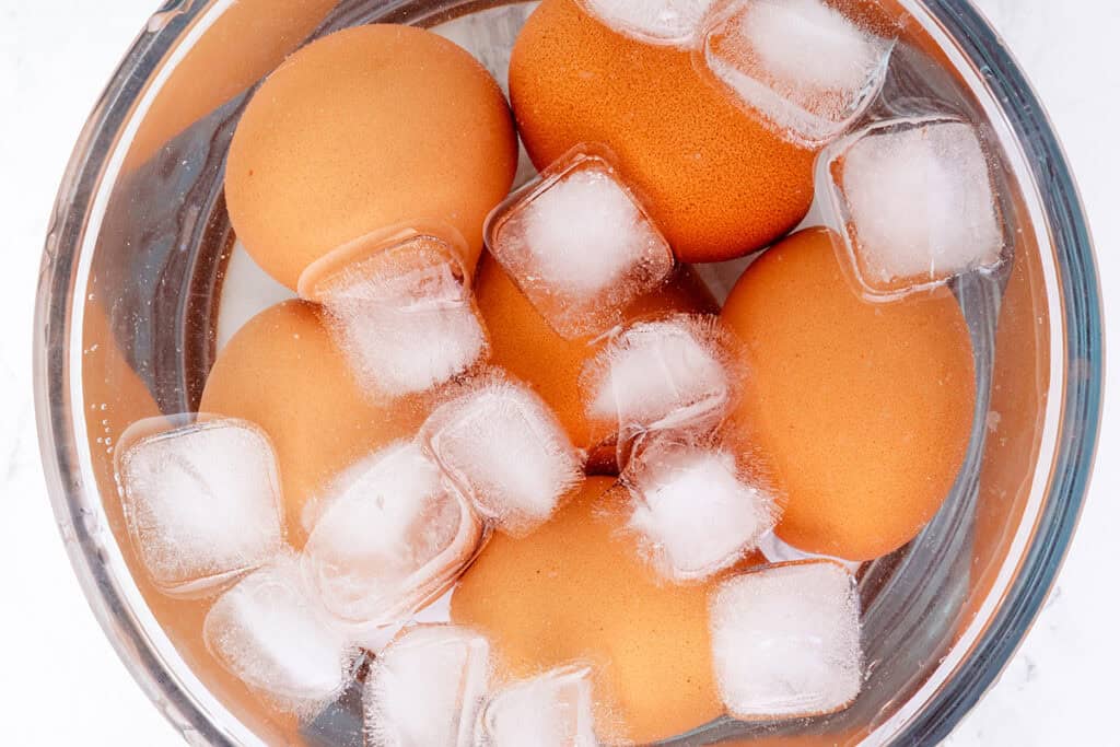 Brown eggs destined for a classic Southern deviled eggs recipe sit submerged in a bowl of ice water. The top-down view clearly reveals the cooling process, essential for achieving perfect hard-boiled eggs.