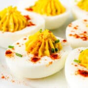 Close-up of Southern deviled eggs on a plate. Halved boiled eggs with creamy yolk filling, sprinkled with paprika and garnished with chopped chives. The vibrant yellow and white contrast with the red paprika, creating an appetizing presentation inspired by traditional Southern recipes.