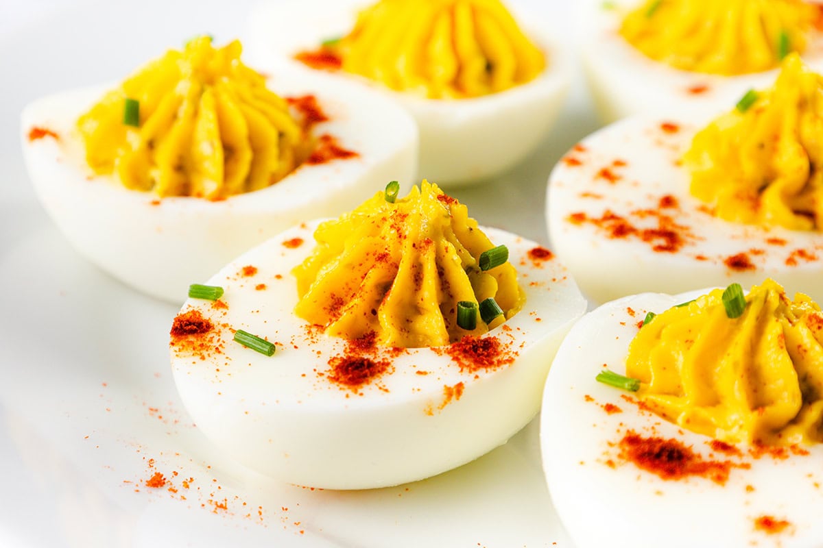 Close-up of Southern deviled eggs on a plate. Halved boiled eggs with creamy yolk filling, sprinkled with paprika and garnished with chopped chives. The vibrant yellow and white contrast with the red paprika, creating an appetizing presentation inspired by traditional Southern recipes.