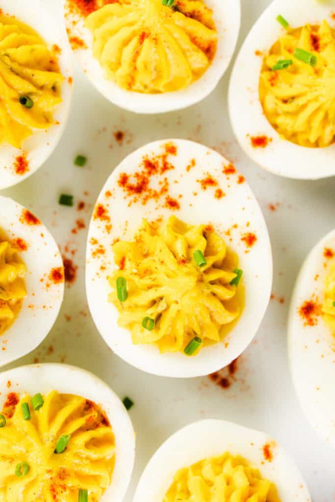 A close-up of Southern deviled eggs on a white surface, topped with paprika and chopped chives. The eggs are halved with a creamy yellow yolk mixture expertly piped on top, embodying the essence of classic Southern recipes.