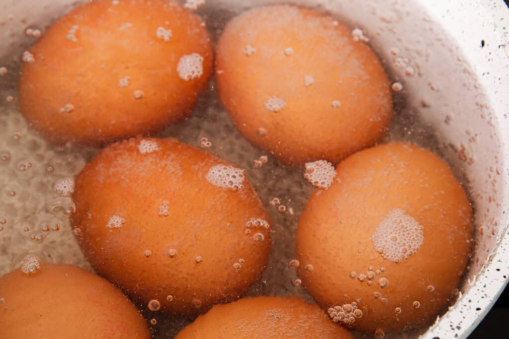Brown eggs are being boiled in water, with small bubbles forming on the surface. The closely packed eggs in the pot are the first step towards a delightful Southern deviled eggs recipe.