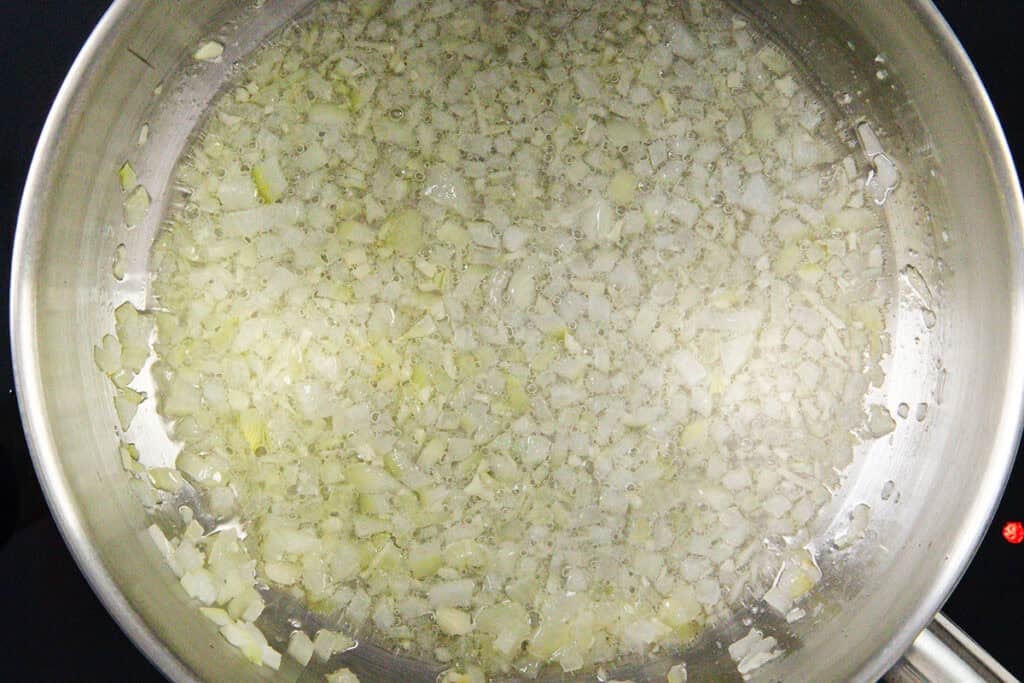 Chopped onions being sautéed in oil in a stainless steel pan, forming bubbles as they cook—the perfect start to Easy Mexican Rice.