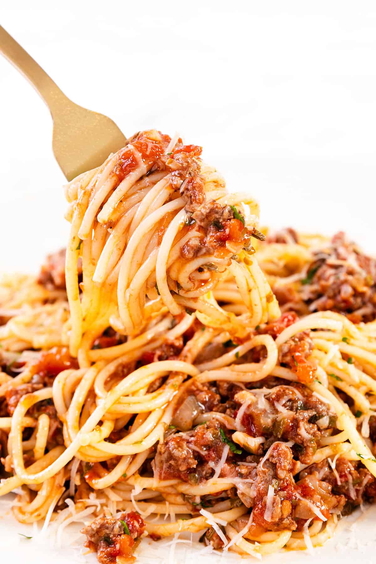 A fork twirls spaghetti topped with chunky bolognese sauce, including ground meat and diced tomatoes, over a plate. Grated cheese can be seen sprinkled on top, adding a finishing touch to the pasta dish.