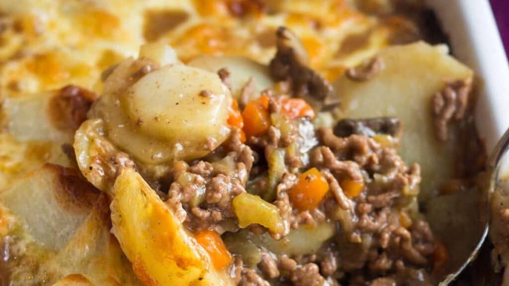 A close-up of a serving of hearty casserole with layers of sliced potatoes, ground beef, carrots, and melted cheese in a creamy sauce—perfect for freezer meals or make ahead meals.