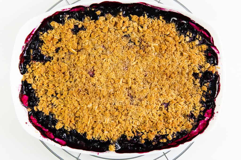 A rectangular baking dish filled with blueberry crumble, featuring a golden-brown oat topping and bubbling purple blueberry dessert filling around the edges.