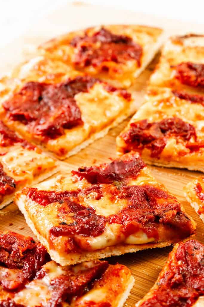 Rectangular slices of Trenton Tomato Pie with melted cheese and tomato sauce rest on a wooden cutting board. The thin, crispy crust features visible browned edges, highlighting this classic pizza style.